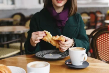 Kobieta podjada pączka przy kawie